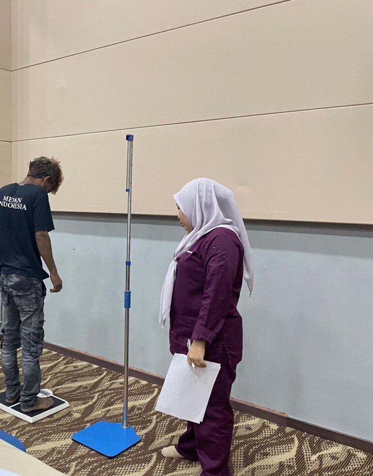 Pekerja menjalani pengukuran berat badan dan ketinggian sambil diperhatikan oleh kakitangan klinik